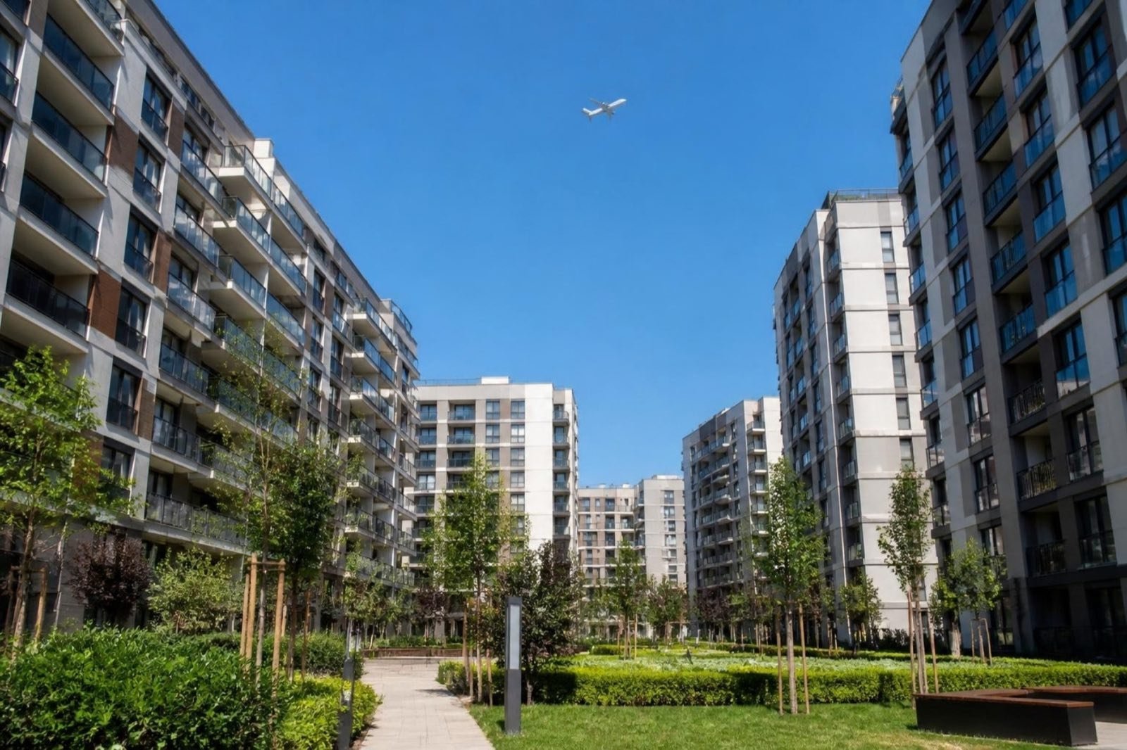 Landscaped courtyard between new apartment blocks, with an airliner high overhead