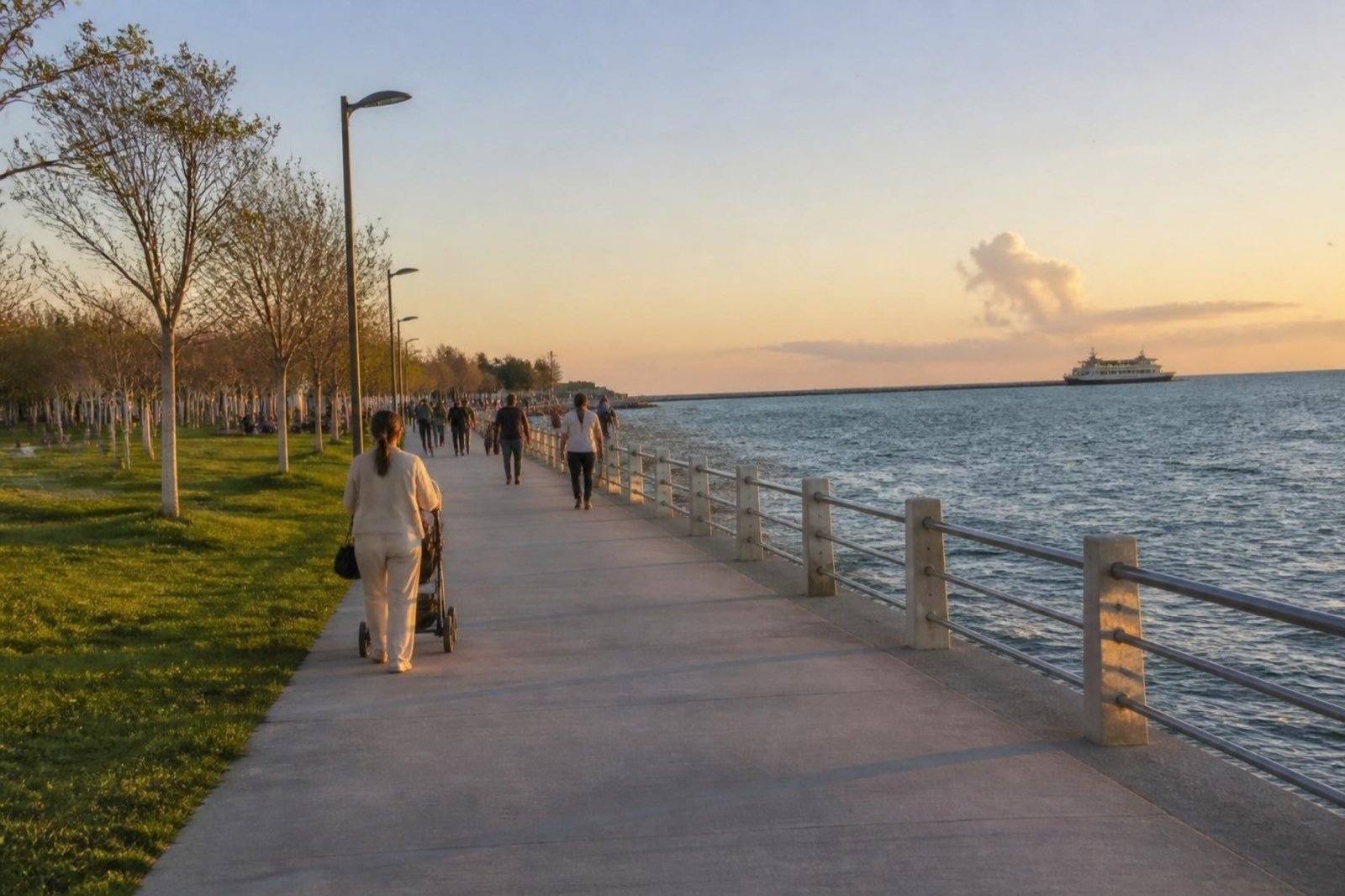 People strolling along a lamp-lit seaside path in the evening, a ferry out at sea